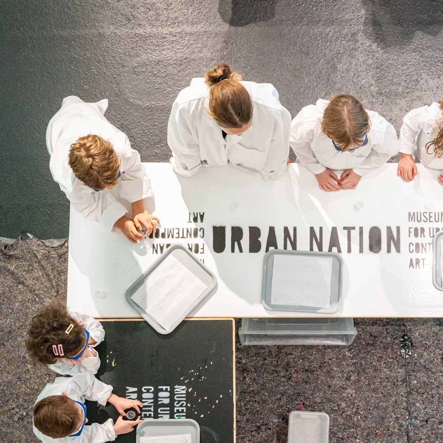 Kinder in weißen Kitteln gestalten Schablonen im Urban Nation Museum