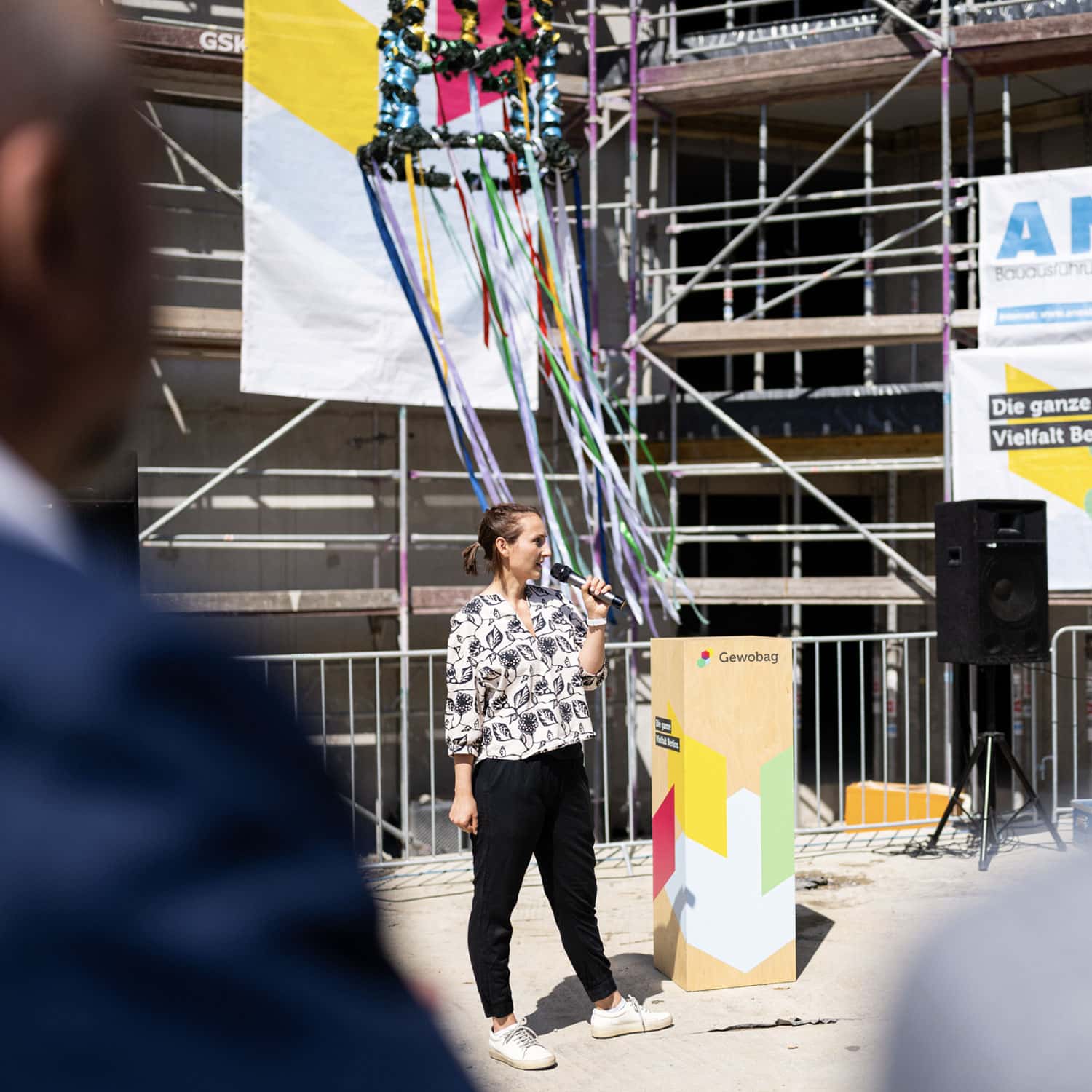 Frau hält eine Rede mit Mikrofon beim Richtfest vor einem Gerüst