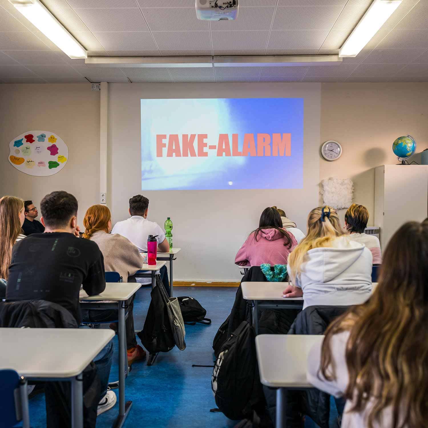 Schulklasse schaut auf eine Projektion „FAKE-ALARM" im Klassenzimmer